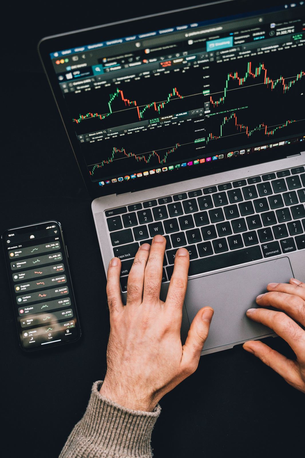 Trader reviewing market charts on a laptop and mobile device